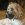 En brun hund sidder på en seng med et KONG Extreme-legetøj i munden.